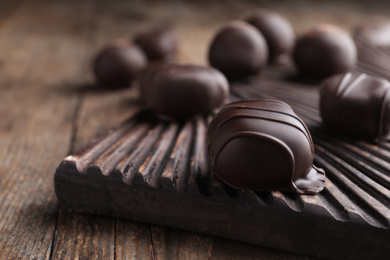 Photo of Tasty dark chocolate candies on wooden board, closeup