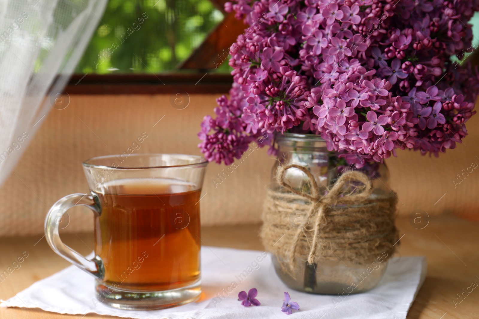 Photo of Bouquet with beautiful lilac flowers and glass cup of tea on wooden table indoors