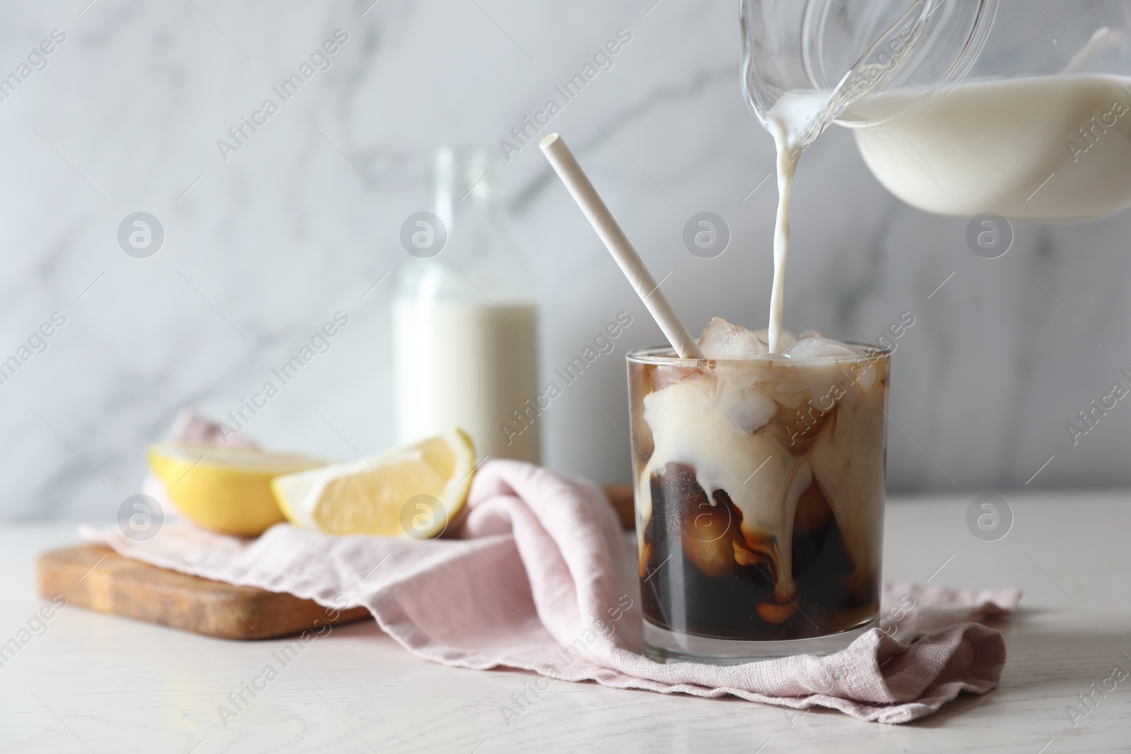 Photo of Pouring milk into glass with refreshing iced coffee at white wooden table, closeup