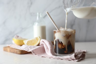 Photo of Pouring milk into glass with refreshing iced coffee at white wooden table, closeup