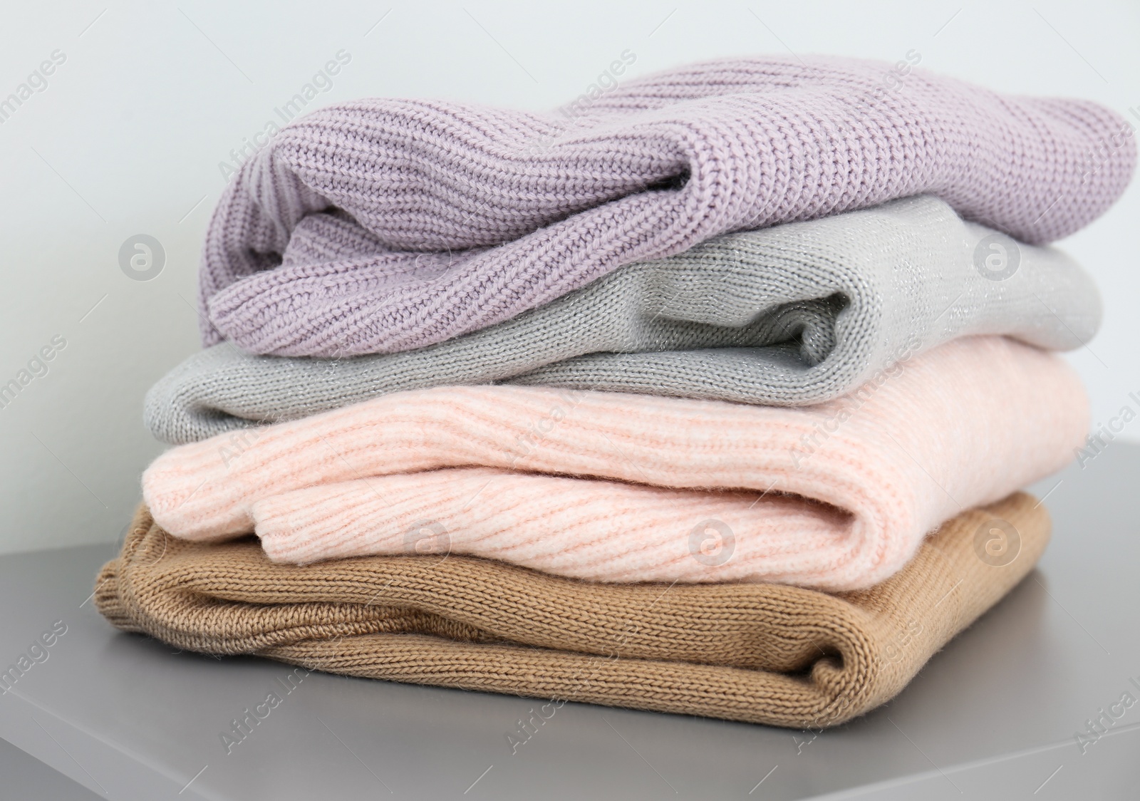 Photo of Stack of folded warm knitted sweaters on grey table