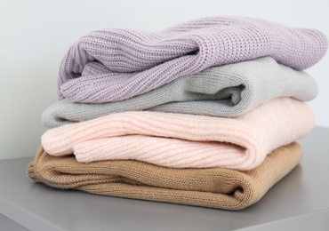 Photo of Stack of folded warm knitted sweaters on grey table