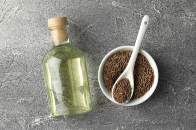 Photo of Caraway (Persian cumin) seeds in bowl and essential oil on light gray textured table, flat lay