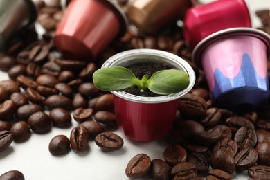 Photo of Coffee capsules with seedling and beans on white marble table, closeup
