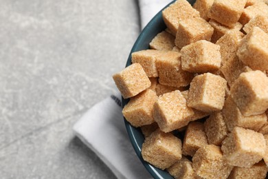Photo of Brown sugar cubes in bowl on light grey table, top view. Space for text