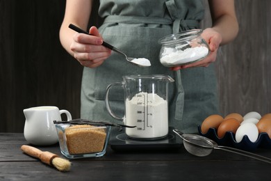 Photo of Woman adding baking powder into measuring cup at black wooden table, closeup