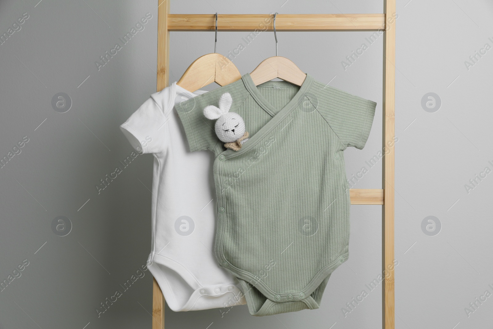 Photo of Baby bodysuits hanging on ladder near light wall