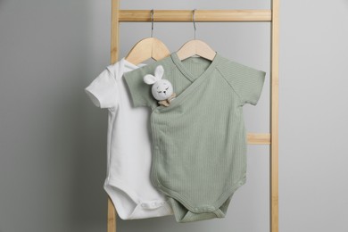 Photo of Baby bodysuits hanging on ladder near light wall