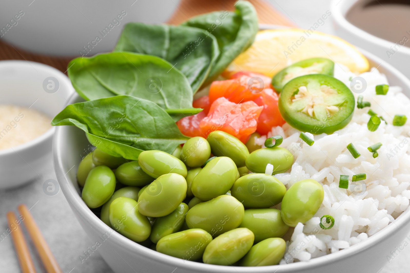 Photo of Poke bowl with salmon, edamame beans and rice on light grey table, closeup