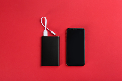 Photo of Mobile phone and portable charger on red background, flat lay