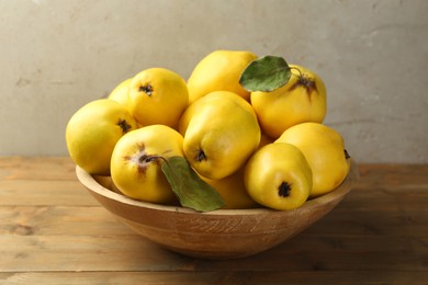 Tasty ripe quince fruits in bowl on wooden table