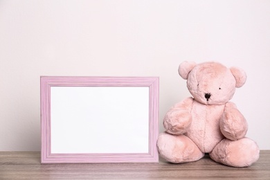 Photo of Photo frame and adorable teddy bear on table against light background, space for text. Child room elements