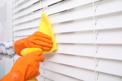 Photo of Woman cleaning window blinds with detergent and rag, closeup