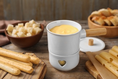 Photo of Pot of tasty cheese fondue and products on wooden table