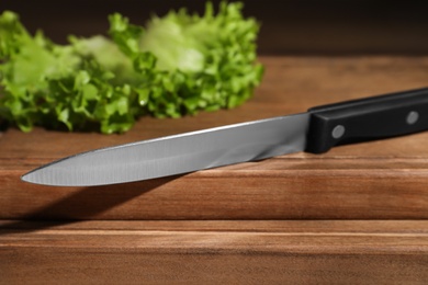 Photo of Utility knife and fresh lettuce leaves on wooden table, closeup. Clean dishes