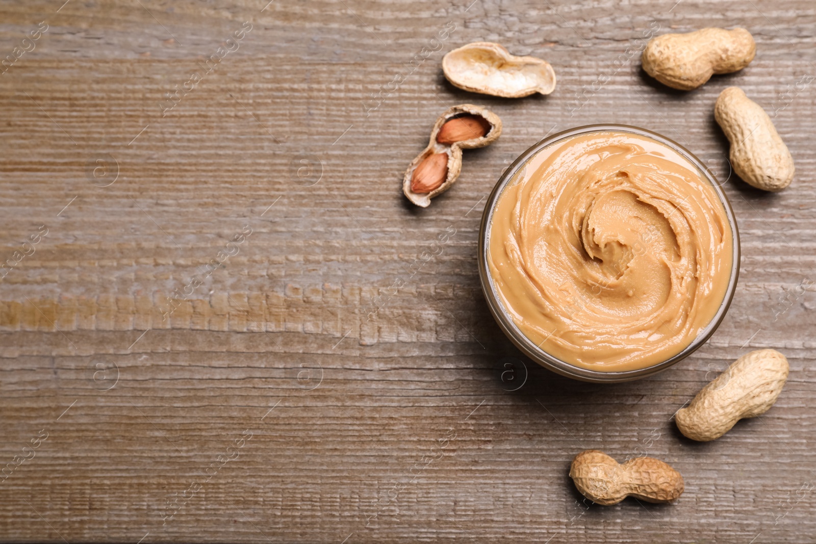 Photo of Yummy peanut butter in glass bowl on wooden table, flat lay. Space for text