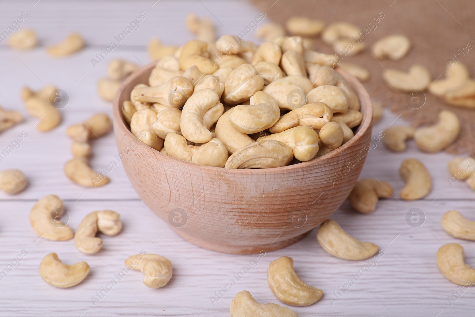 Photo of Tasty cashew nuts in bowl on white wooden table, closeup