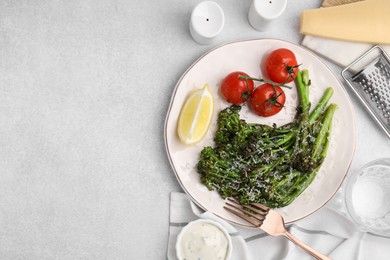 Tasty cooked broccolini with cheese, tomatoes and lemon on light table, flat lay. Space for text