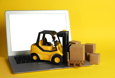 Photo of Laptop, forklift model and carton boxes on yellow background. Courier service
