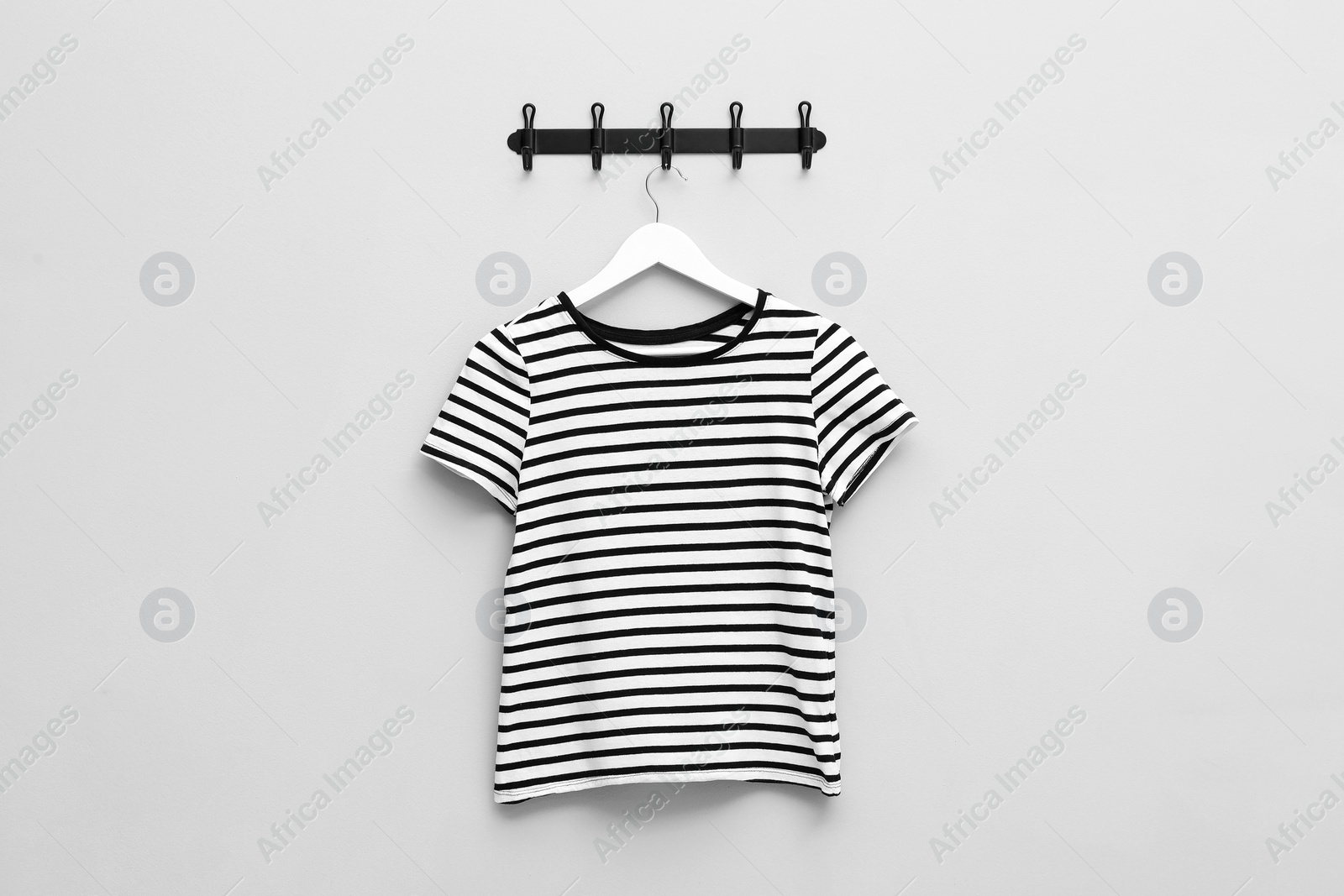 Photo of Hanger with striped T-shirt on light grey wall