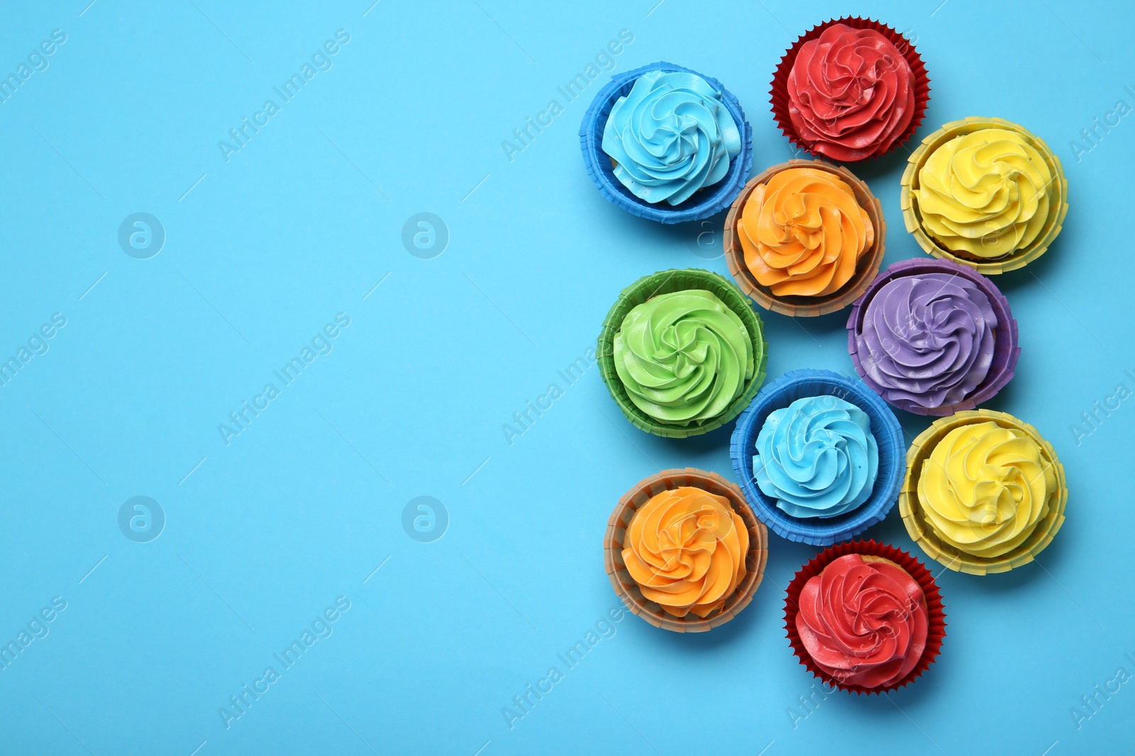 Photo of Many tasty cupcakes with bright cream on light blue background, flat lay. Space for text