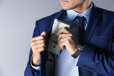 Photo of Man putting bribe into pocket on grey background, closeup