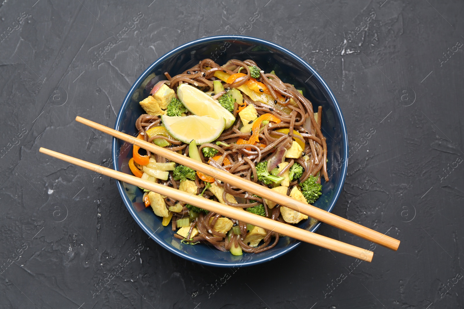 Photo of Stir-fry. Delicious cooked noodles with chicken and vegetables in bowl served on gray textured table, top view