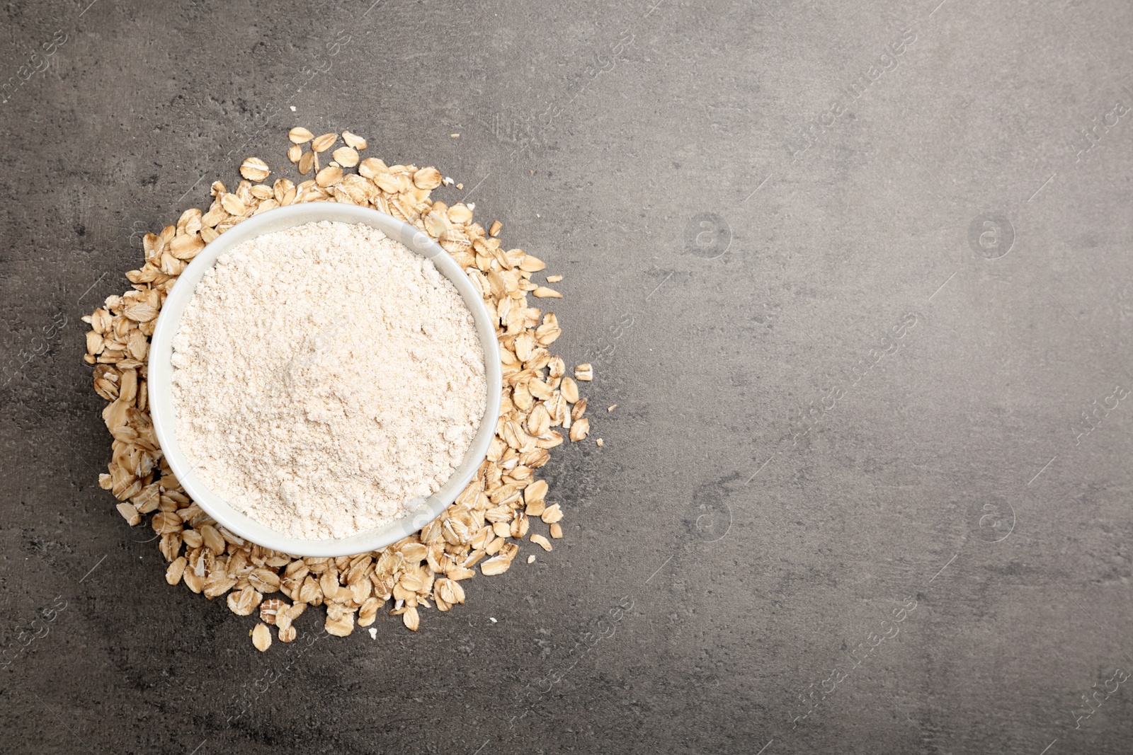 Photo of Bowl with oat flour and flakes on grey background, top view. Space for text