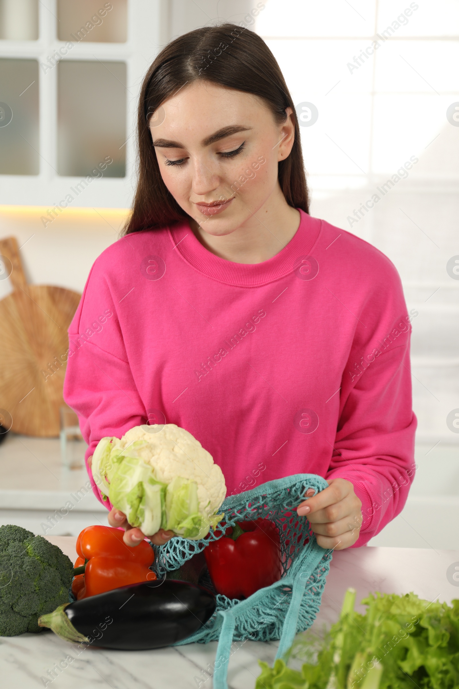 Photo of Woman taking cauliflower out from string bag at light marble table in kitchen