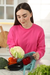 Photo of Woman taking cauliflower out from string bag at light marble table in kitchen