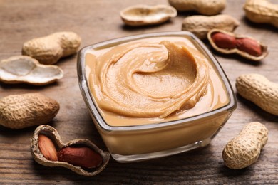 Yummy peanut butter in glass bowl on wooden table, closeup