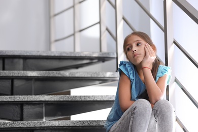 Photo of Depressed preteen girl sitting alone on stairs. Space for text