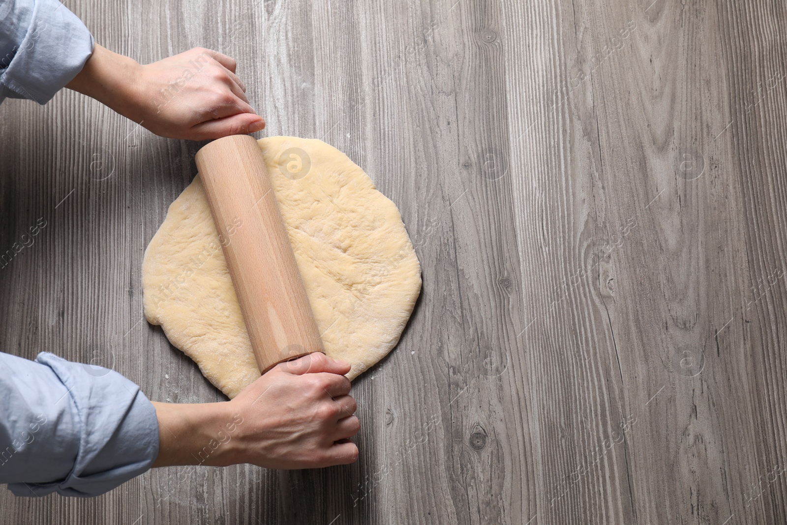 Photo of Woman rolling raw dough at wooden table, top view. Space for text