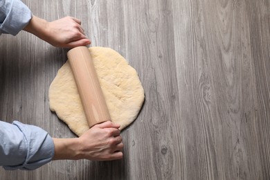 Woman rolling raw dough at wooden table, top view. Space for text