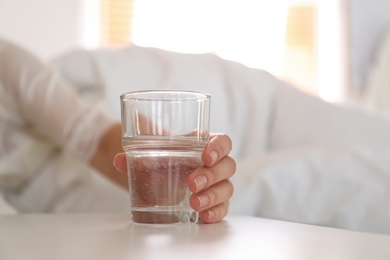 Woman taking glass of water from nightstand in bedroom, closeup