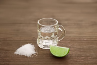 Photo of Mexican tequila shot with lime slice and salt on wooden table, closeup. Drink made from agave