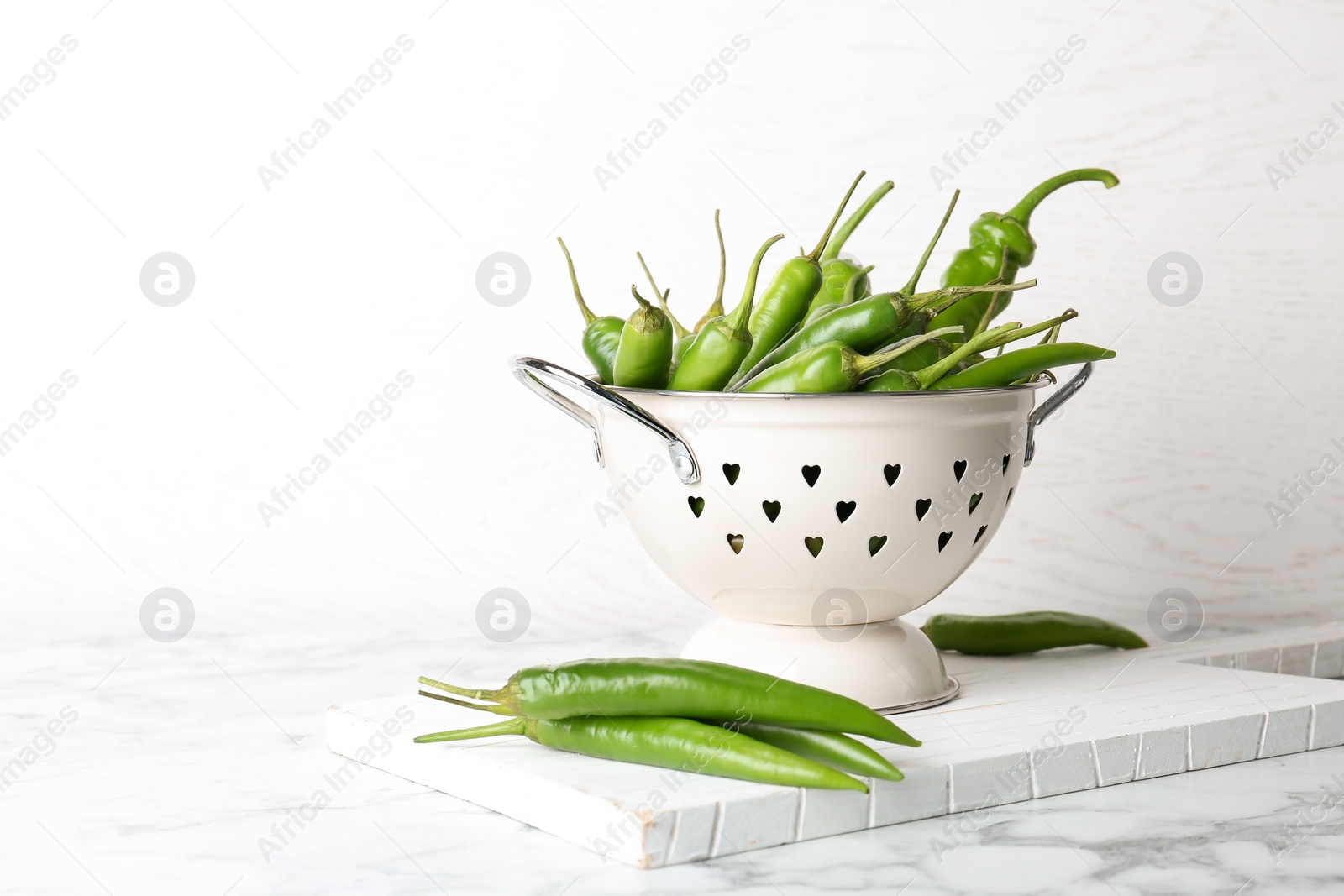 Photo of Colander with ripe chili peppers on table