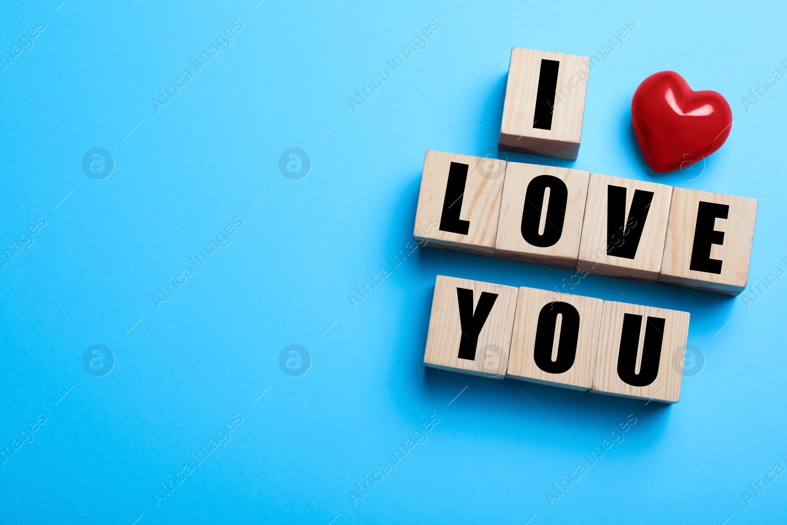 Photo of Cubes with words I Love You and red heart on light blue background, flat lay. Space for text