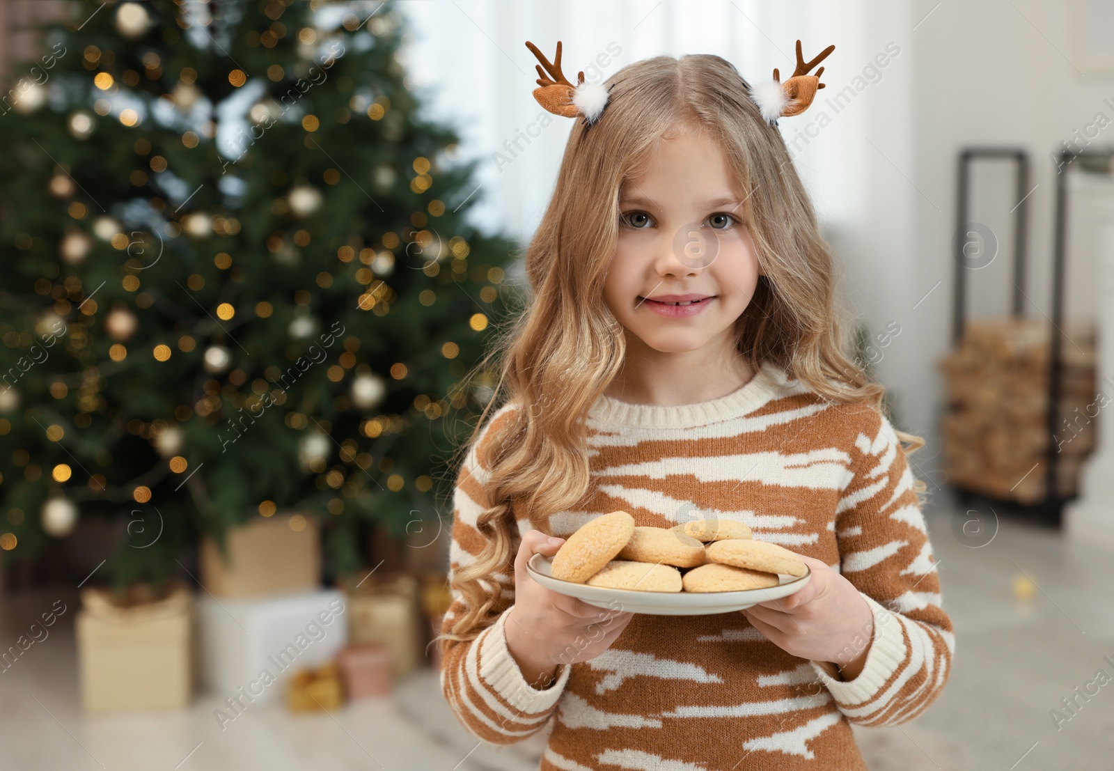 Photo of Portrait of cute little girl in Christmas hair clips holding plate with cookies at home