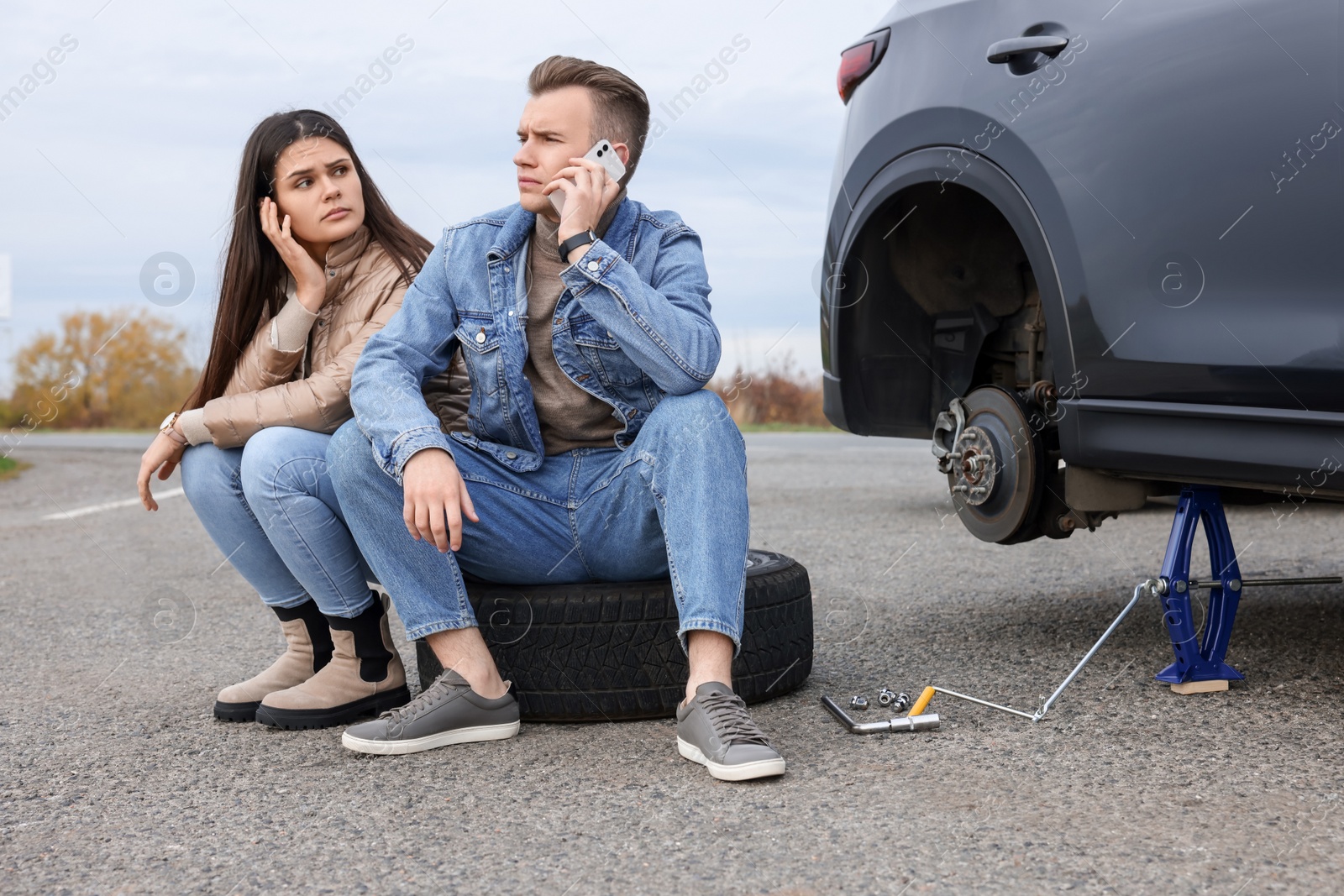 Photo of Young man calling to car service on roadside. Tire puncture