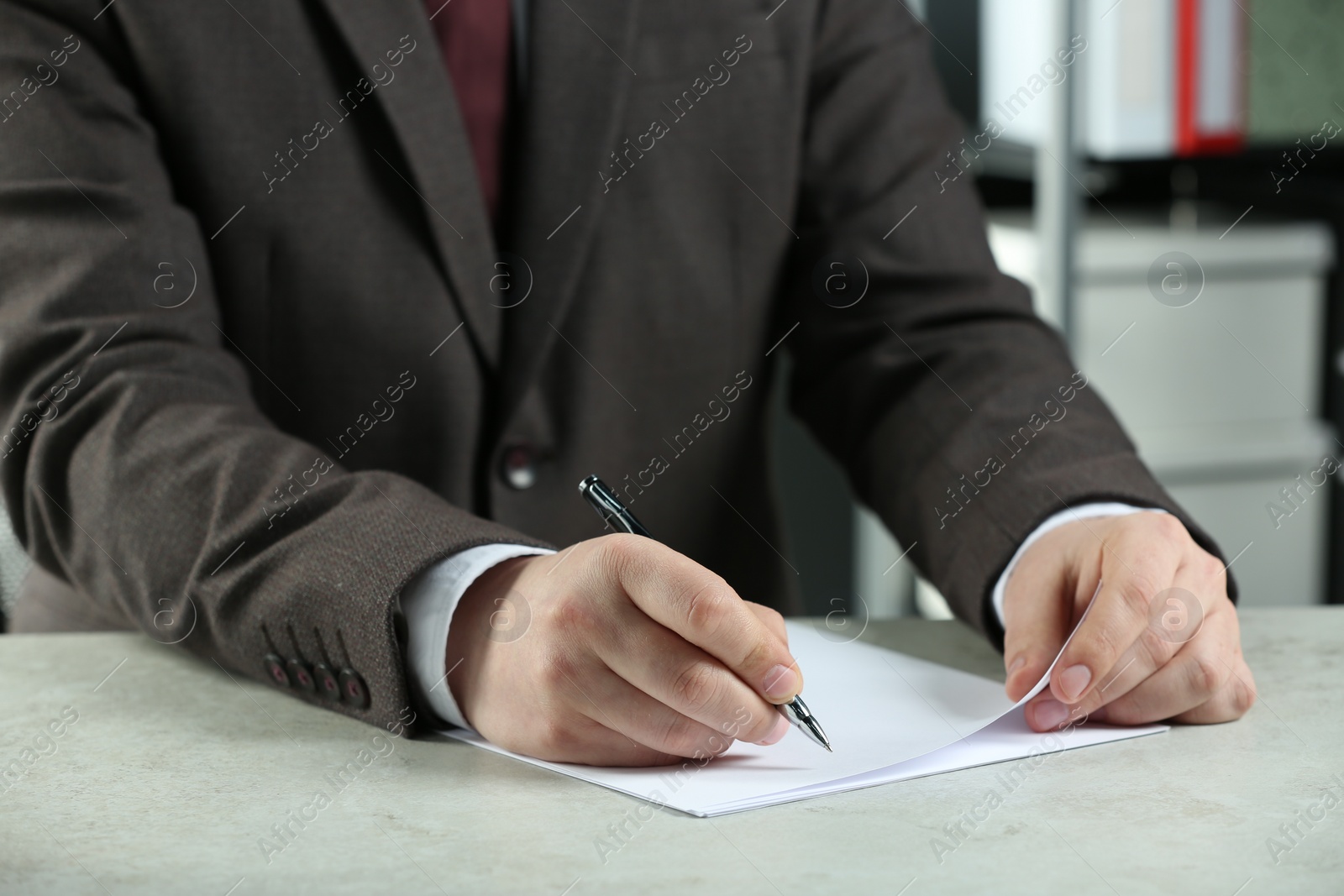 Photo of Man writing on sheet of paper with pen at white table indoors, closeup