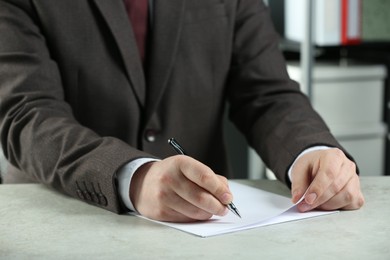 Man writing on sheet of paper with pen at white table indoors, closeup