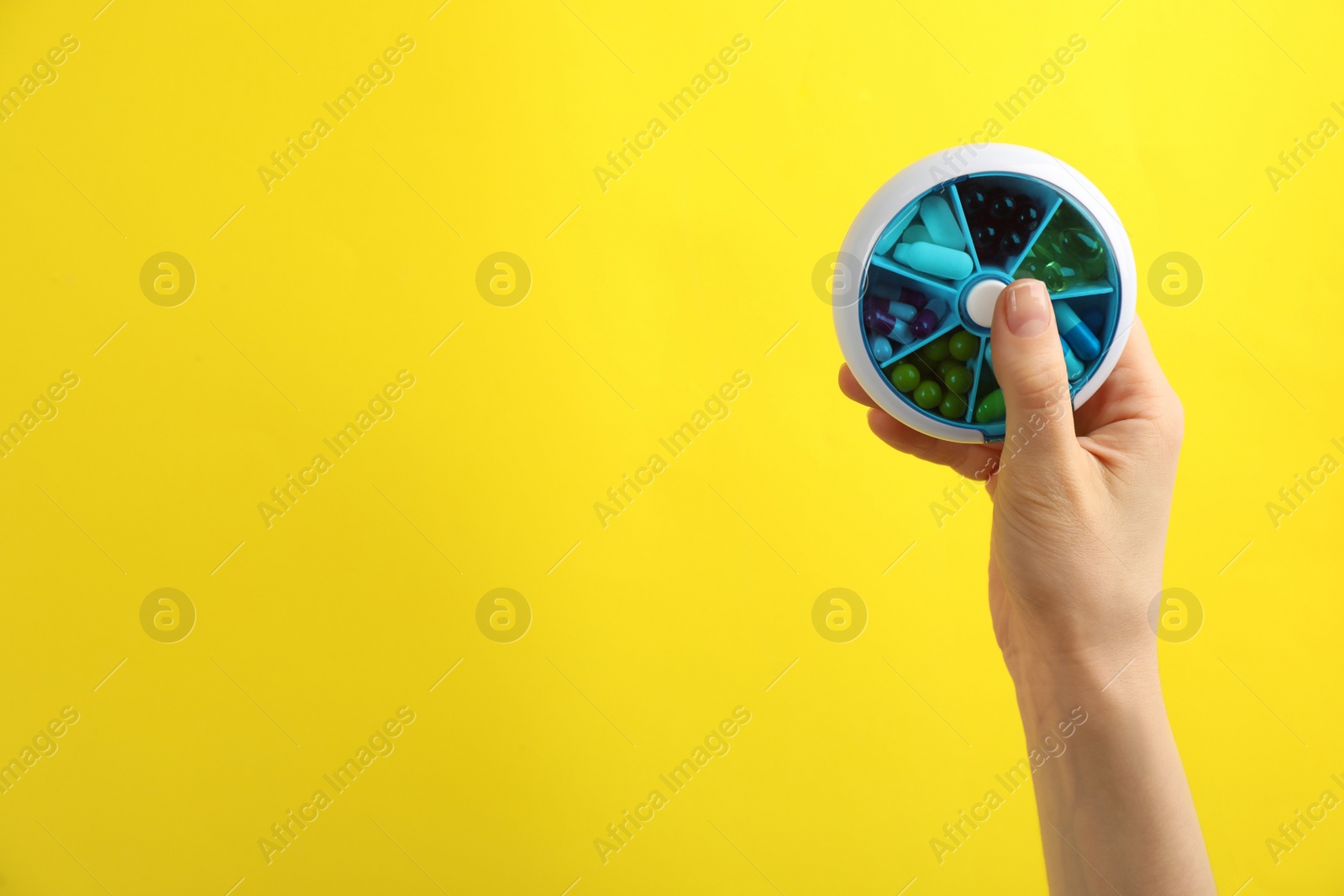 Photo of Woman holding plastic box with different pills on yellow background, closeup. Space for text