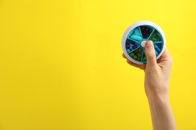 Woman holding plastic box with different pills on yellow background, closeup. Space for text