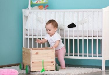 Photo of Cute baby holding on to wooden cart in children room. Learning to walk
