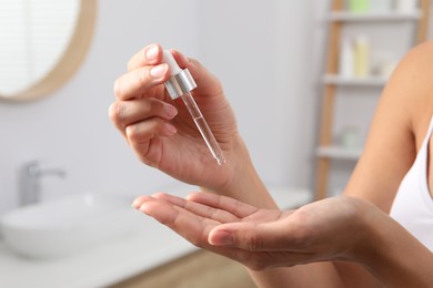 Woman applying cosmetic serum onto her hand indoors, closeup