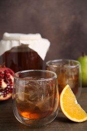 Photo of Tasty kombucha with ice cubes and fruits on wooden table