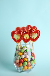 Photo of Delicious heart shaped lollipops and dragees in glass on turquoise background. Space for text