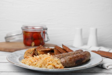 Plate with sauerkraut, sausages and potatoes on white wooden table