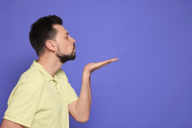 Photo of Handsome man blowing kiss on violet background. Space for text